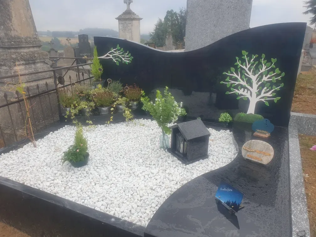 Monument funéraire design en granit noir et graviers blancs dans un cimetière.